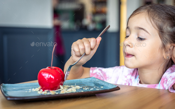 A little girl eats a cherry-shaped chocolate mousse, an unusual cherry cake.