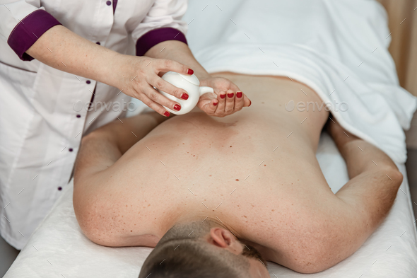 Female hands do a back massage to a man in the salon. Stock Photo by puhimec