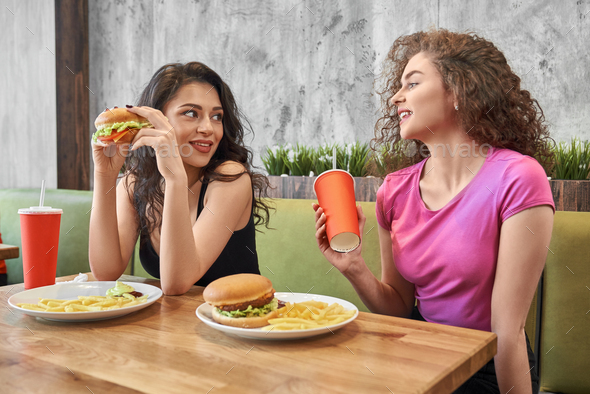 Female friends communicating while eating hamburgers in cafe