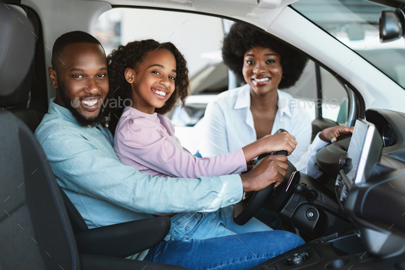 Happy black family buying new car, test driving automobile, smiling at camera in auto dealership