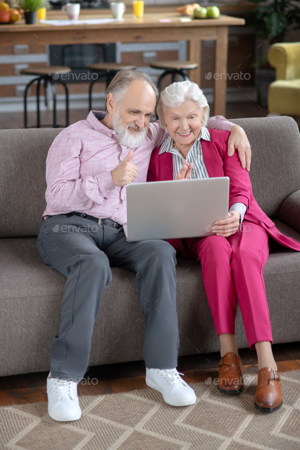Elderly married couple sitting on the sofa and having video call
