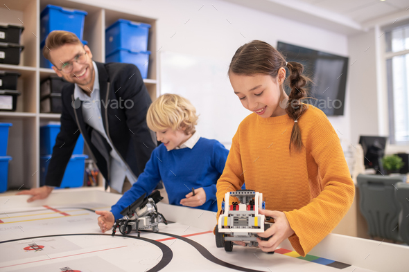 Pupils playing with buildable cars, teacher watching them happily