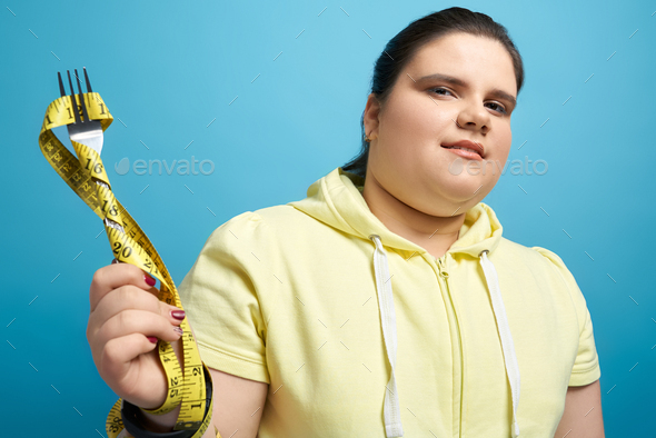 Pretty fat lady keeping fork wrapped by measuring tape