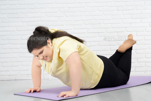 Brunette fat girl is trying to do push ups in mat indoors