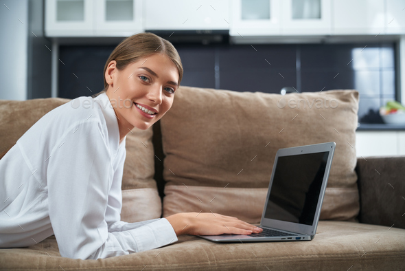 Beautiful woman lying on couch with wireless laptop