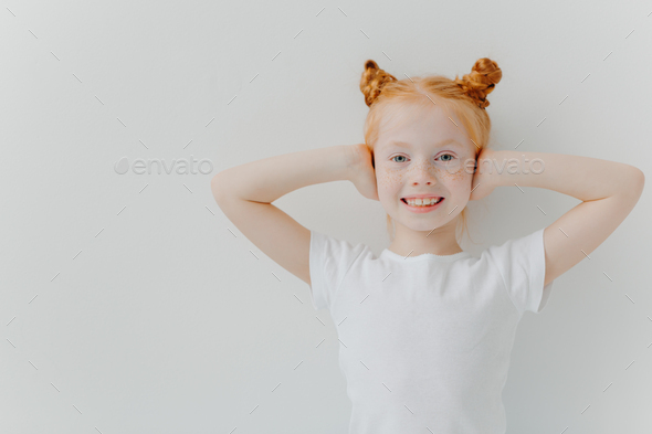 Glad smiling girl covers ears with hands, ignores noise, has two ginger buns
