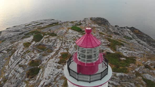 Slow aerial orbit of red bricklight lighthouse in Norway as the sun starts to go down alt