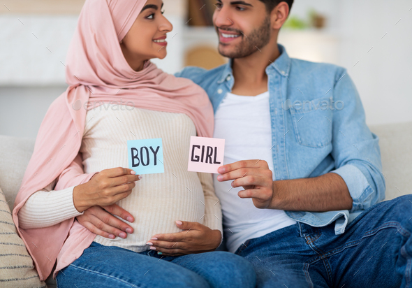 Gender reveal concept. Happy arab couple holding boy and girl sticker cards in pink and blue colors
