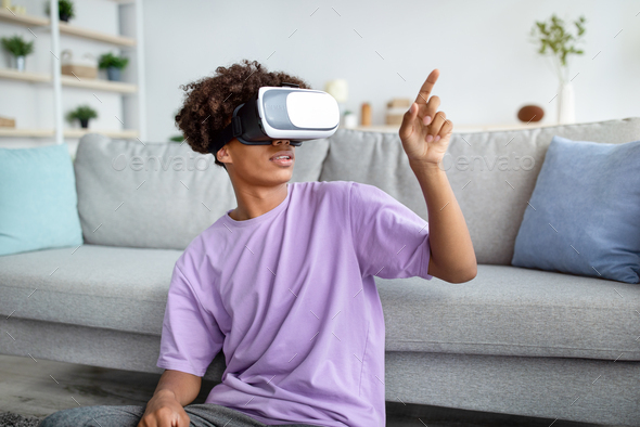 Black teen guy in VR headset exploring virtual at touching imaginary screen Stock by Prostock-studio