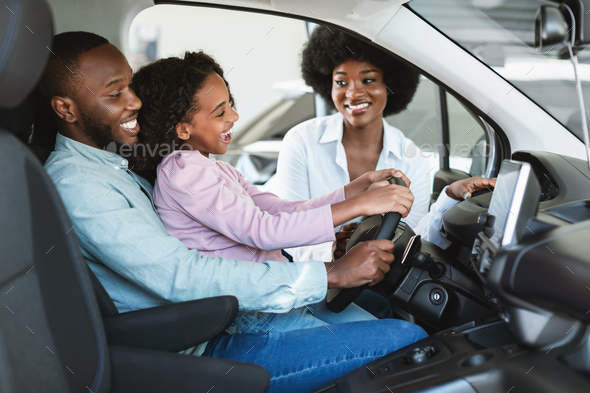 Cheerful black family sitting in new car, going on test drive, buying automobile at dealership