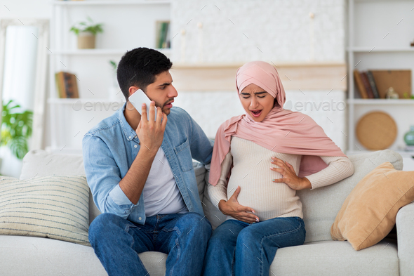 Worried arab husband calling doctor or ambulance while his pregnant wife having labor pains and