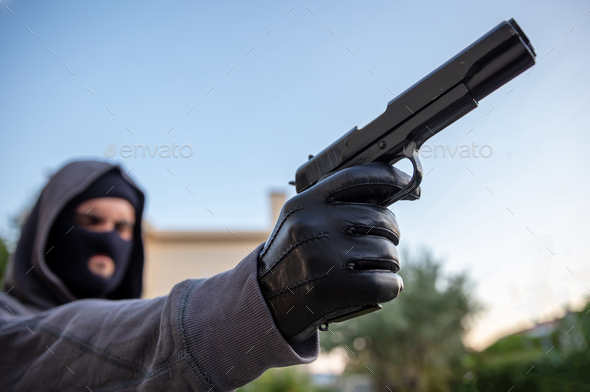 Hooded robber holding a pistol, blur nature background,
