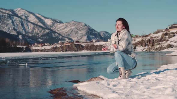 Woman Tourist Sits on the Bank of a River in a Mountainous Area alt