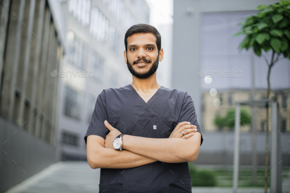 Arabian doctor, wearing gray medical scrubs, looking at camera, standing outdoors