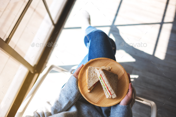 a woman holding two pieces of whole wheat sandwich in wooden plate