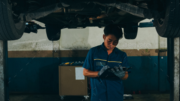 Professional car mechanic using paperwork makes the oil and engine check to the car.