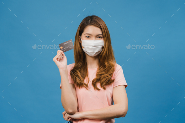 Young Asia lady wearing medical face mask show credit bank card with positive expression.
