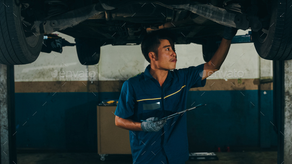 Professional car mechanic using paperwork makes the oil and engine check to the car.
