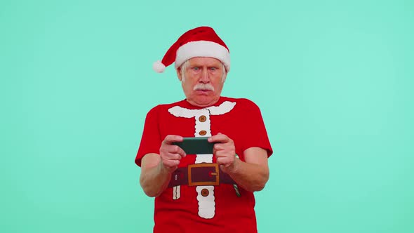 Worried Grandfather in Christmas Tshirt Enthusiastically Playing Racing Video Games on Mobile Phone alt