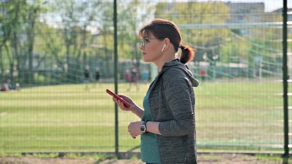 Active Mature Woman in Sportswear with Smartphone Outdoor Profile View alt