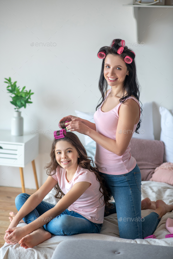 Mom with hair curlers curling hair to her daughter