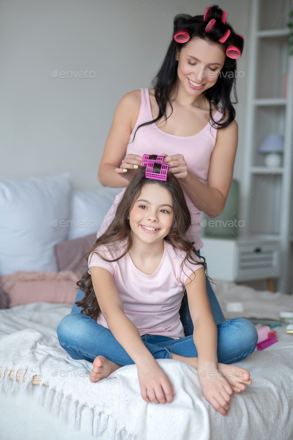 Young mom with hair curlers curling hair to her daughter
