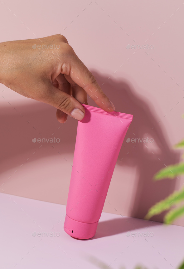 A pink tube with a cosmetic product on a pink background. Mockup cream for face and body.