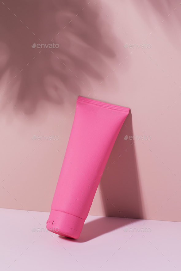 A pink tube with a cosmetic product on a pink background. Mockup cream for face and body.