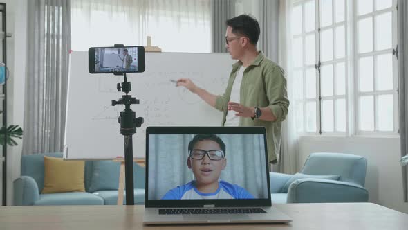 Asian Male Teacher Teaching Math Online At Home With Boy Student On Laptop Screen alt