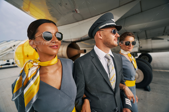 Aviator in sunglasses and female flight attendants going ahead