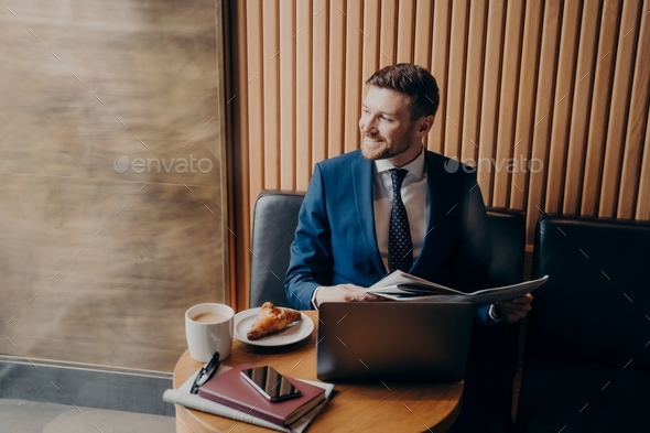 Business man looking outside window in cafe while holding newspaper