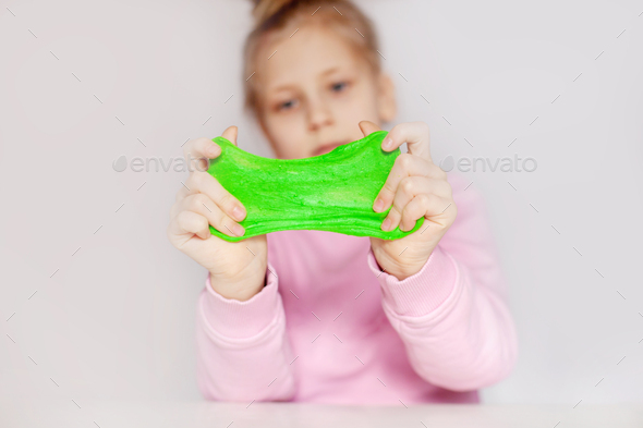 Cute girl playing with green slime. The girl holds in her hands and ...