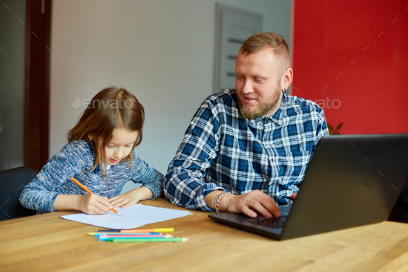 Father working in his home office on a laptop, her daughter sits next to her and draw