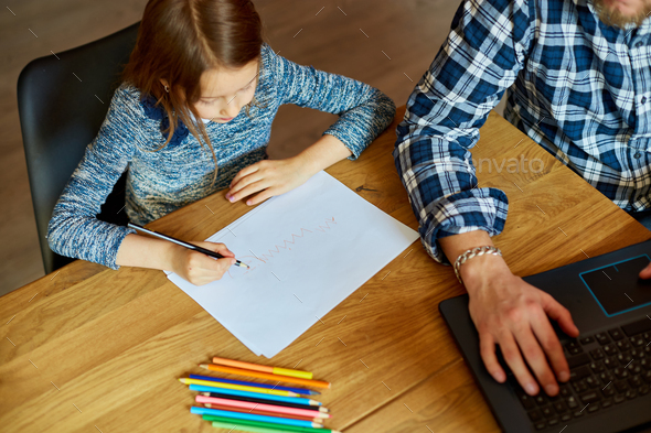Top view of Father working in his home office on a laptop, her daughter sits next to her and draw
