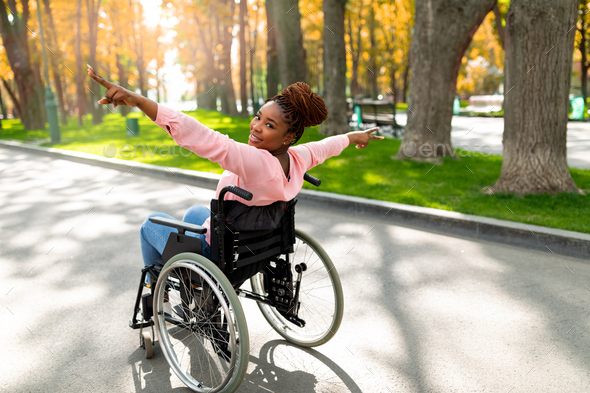 Young disabled black woman in wheelchair spreading arms, making victory gesture, feeling free at