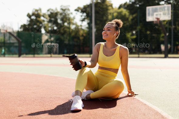 Portrait of sporty black woman in yellow sportswear drinking water