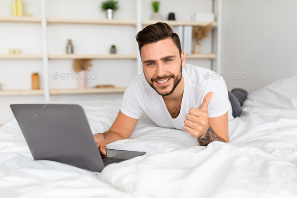I like distant job. Millennial man with laptop computer gesturing thumbs up, working online, lying
