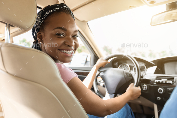 Confident black woman driving car, smiling at camera