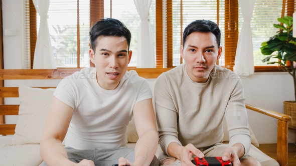 gay couple sit on couch use joystick controller play video game spend fun time together.