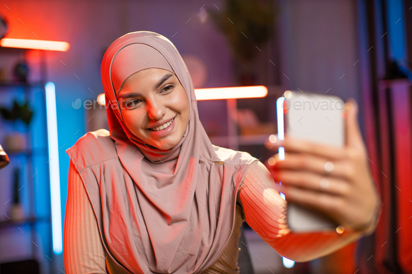 Adorable woman in hijab using mobile for taking selfie Stock Photo by ...