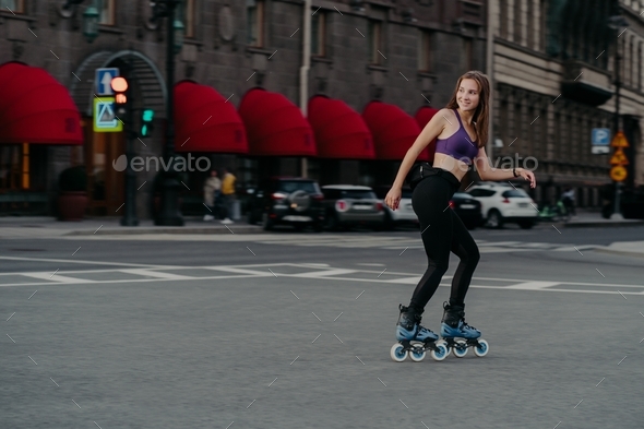 Active slim woman dressed in cropped top and leggings rollerblades through city