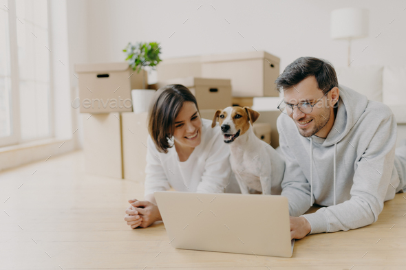 Husband and wife watch film online on laptop, their domestic animal poses between