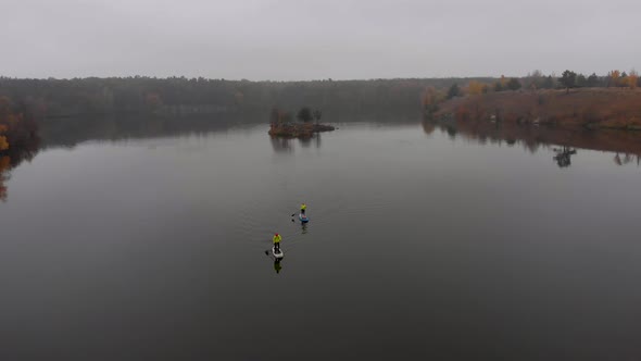 Drone Shot of Man and Woman on Sup Paddle Boards at Wide River on Golden Autumn Forest Background alt