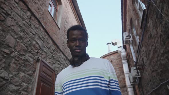 A Young Black Student with Headphones Walks Through the City Centre at Sunset