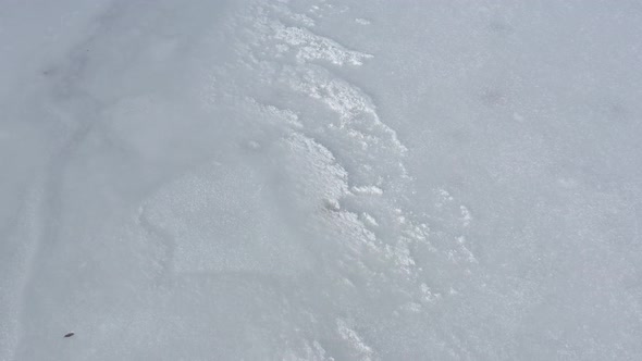 Snow and ice on frozen lake surface 4K drone footage alt