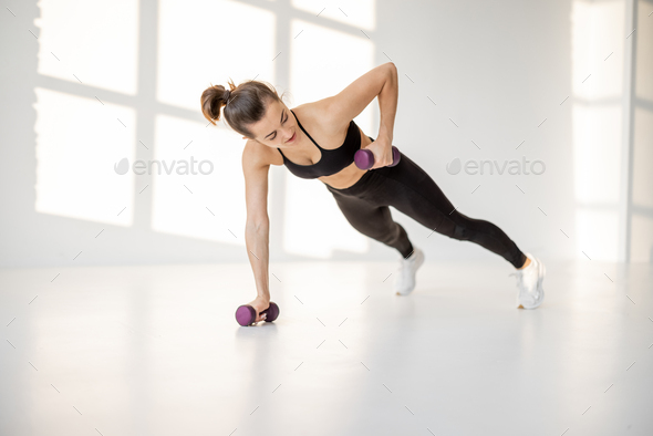 Woman doing cardio with dumbbells at white room