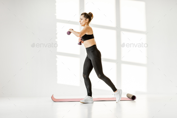 Woman doing cardio with dumbbells at white room