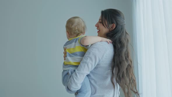 Caucasian loving mother tosses cute baby boy child up with happiness in living room. alt