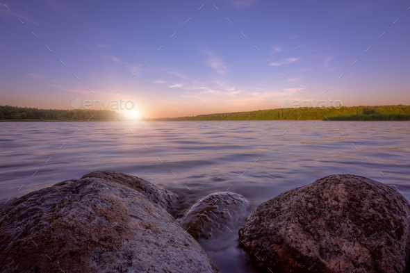 Small boulders submerged in water of a lake on a lakeshore at dusk - Stock Photo - Images