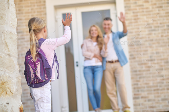 Girl with backpack waving goodbye to parents